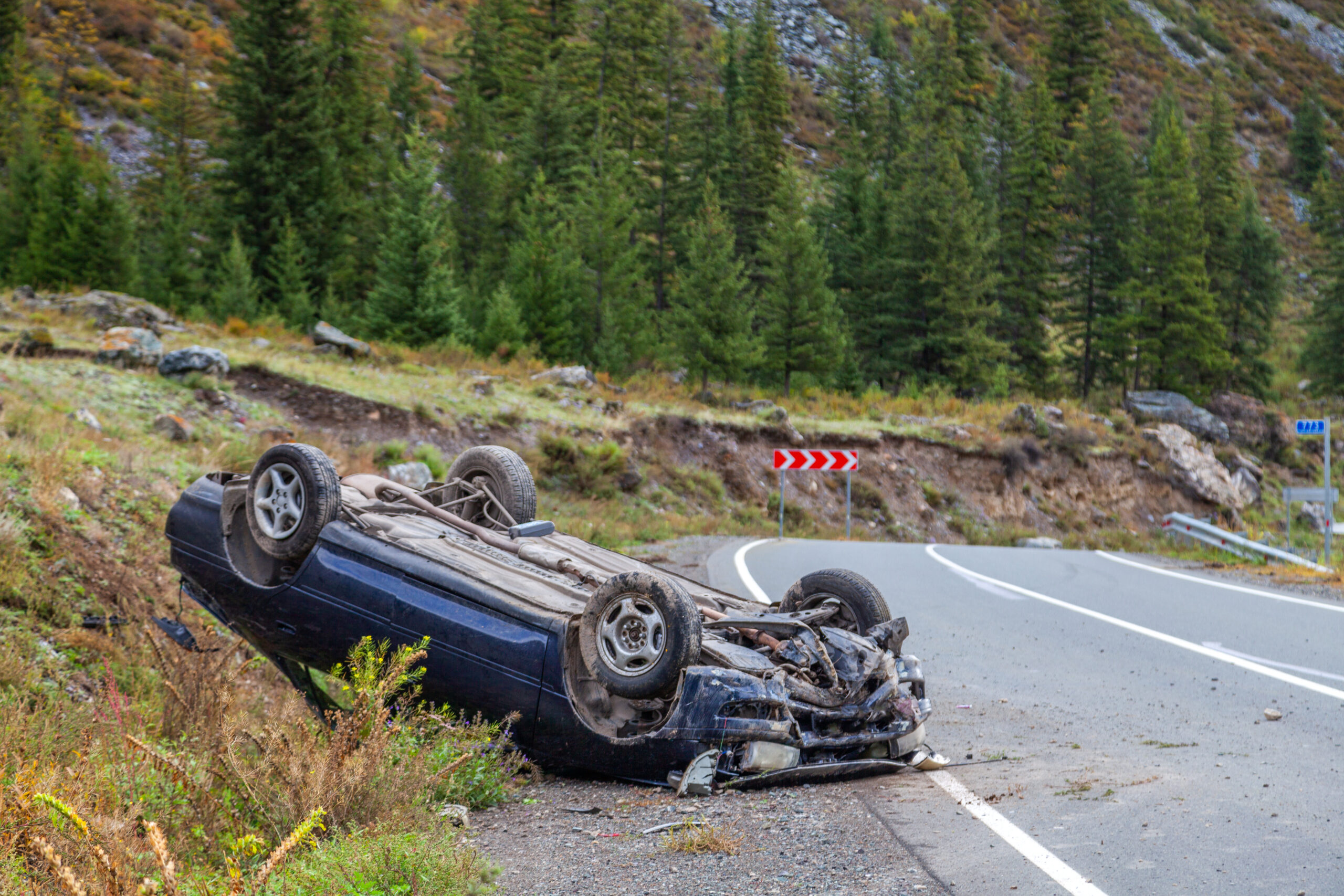 Car accident place on a bend, overturned car lies on the roof, broken bumper, glass, mountain road background, horizontal, copy space